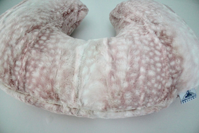 May include: A pink and white faux fur U-shaped pregnancy pillow with a white label that says "Dreamin' Grace Designs".
