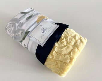 May include: A white and gray floral patterned blanket with a yellow fluffy blanket underneath. The floral blanket has a tag that says "Brooklyn Grace Designs".