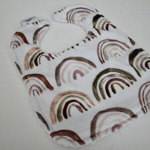 May include: White baby bib with a brown, pink, and green watercolor rainbow pattern.