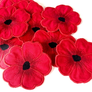 May include: A collection of red fabric poppy flower patches, each featuring five rounded petals and a textured black circular centre. The embroidery details radiate from the centre of each flower, creating a layered arrangement of individual floral appliqués.