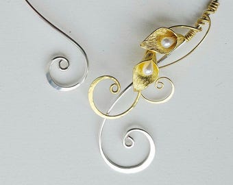 May include: A silver-toned collar necklace with gold accents. The necklace features a delicate design with two gold-colored leaf-shaped elements, each holding a small, round pearl. The design includes elegant swirls.