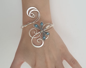 May include: Silver wire bracelet with a dragonfly design featuring blue gemstones.