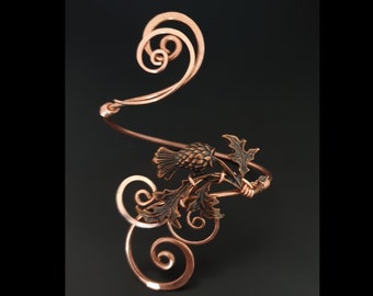 May include: Copper wire arm cuff with a stylized thistle design. The cuff is made of copper wire and features a delicate, intricate design. The thistle is a traditional symbol of Scotland.
