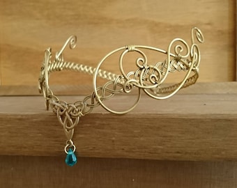 May include: A gold wire headband with a Celtic knot design and a dangling teal blue gemstone.