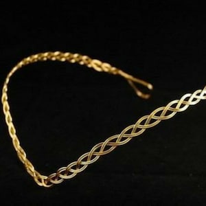 May include: A gold braided headband with a simple design. The headband is made of metal and has a delicate, feminine look.