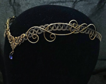 May include: A gold wire headband with a delicate, intricate design. The headband features a small, dangling blue gemstone.
