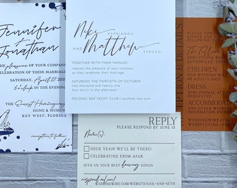 May include: Wedding invitation suite featuring a central invitation card with names and event details in elegant script. Additional cards include a reply card, and details card. A cork, a ring box, and greenery complete the arrangement.