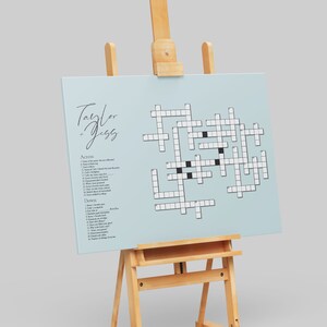 May include: A light blue crossword puzzle on an easel with the text "Taylor + Jess" at the top. The puzzle has a list of clues for "Across" and "Down" on the left side.