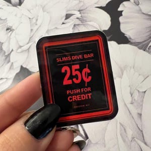 May include: A black and red rectangular sticker with the text "SLIMS DIVE BAR" at the top and "25¢" in the center. Below the price is "PUSH FOR CREDIT". The sticker has a red border.