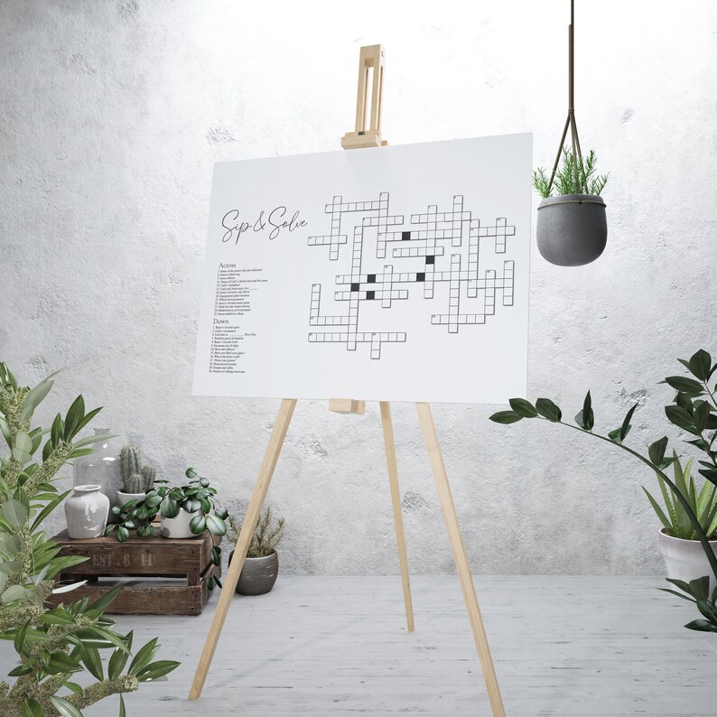 May include: A white crossword puzzle on an easel with the title "Sip & Solve". The puzzle is set up with black squares for the clues and white squares for the answers. The puzzle is on a white background.