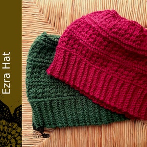 May include: Two crocheted hats, one green and one red, are displayed on a woven surface. The hats have a textured stitch pattern.
