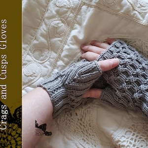 Op de afbeelding: Grijze gebreide vingerloze handschoenen met een textuurpatroon. De handschoenen worden gepresenteerd op een oppervlak met patronen. De afbeelding bevat de tekst "Knit Pattern Crags and Cusps Gloves".