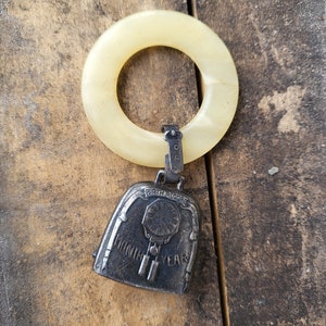 May include: A vintage baby rattle with a white plastic ring and a silver bell. The bell has the words "Birth Record" and "Month Year" engraved on it.
