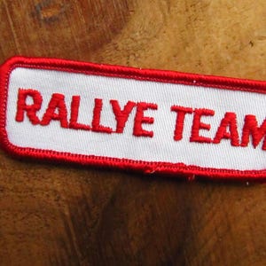 May include: Red embroidered patch with white background and the text "Rallye Team" in red.