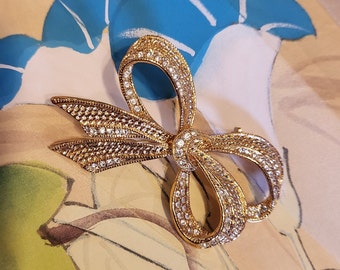 May include: A gold-toned bow brooch with clear rhinestones. The bow is made of metal and has a detailed design.