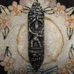 May include: A gold-toned metal door handle with an ornate design featuring a figure in a warrior pose. The handle is surrounded by floral motifs and has a detailed, textured surface.