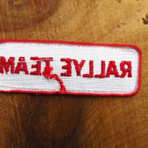 May include: White fabric patch with red embroidered text that reads "Rallye Team".