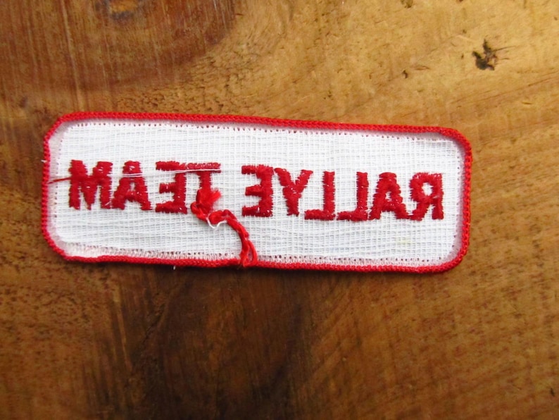 May include: White fabric patch with red embroidered text that reads "Rallye Team".