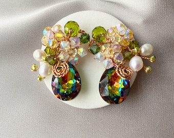 May include: A pair of dangle earrings with a teardrop-shaped iridescent green and gold crystal. The earrings are adorned with small green, white, and gold beads.