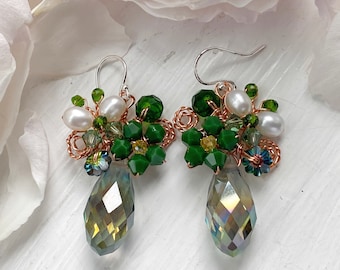 May include: A pair of green and white dangle earrings with teardrop-shaped crystals. The earrings feature a cluster of green and white beads, including faux pearls.