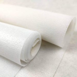 Puede incluir: Se muestran dos rollos de papel blanco texturizado, uno parcialmente desenrollado. El papel tiene una calidad ligeramente translúcida y una textura sutil, similar a la tela. Los rollos están bien enrollados, lo que sugiere un suministro de arte o artesanía.