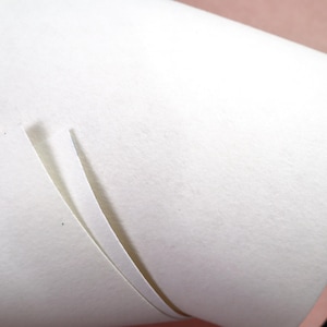 Puede incluir: Primer plano de un rollo de papel blanco con superficie texturizada. Una fina ranura vertical revela las capas internas. El fondo es rosa suave y negro.
