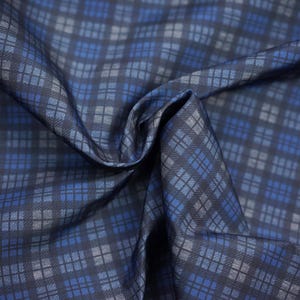 May include: Close-up of a folded fabric with a repeating diamond and square pattern. The fabric features a color palette of navy, light blue, and gray. The fabric has a slight sheen, suggesting a smooth texture.