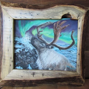 May include: A framed painting of a reindeer with antlers against a backdrop of the aurora borealis. The painting is in a rustic wooden frame.