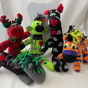 May include: A collection of handmade sock animals, including a red reindeer, a green monster, a black horse with a Star Wars theme, and a zebra with a Halloween theme. Each animal has unique details and colors.