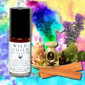 May include: A Wild Child oil perfume bottle with a black lid and a white label listing ingredients such as patchouli, cedarwood, and vanilla. The image includes a candle, flowers, and wood sticks, suggesting a natural fragrance theme.