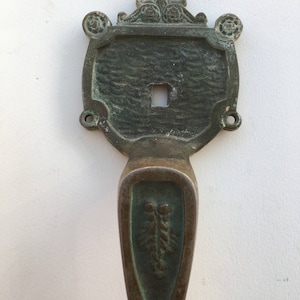 May include: Antique brass door handle with a decorative design. The handle has a square keyhole and a decorative floral design at the top.