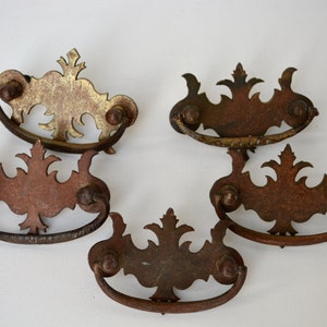May include: Five antique drawer pulls with ornate designs. The pulls are made of metal and have a distressed finish. Some of the pulls are gold, while others are a rusty brown color.