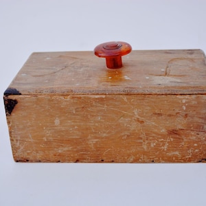 May include: A wooden box with a dark brown stain and a red plastic knob on the lid.