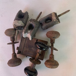 May include: A collection of vintage hardware items including door knobs, a door lock, and ceramic electrical insulators. The door lock is labeled "RUSSWIN".
