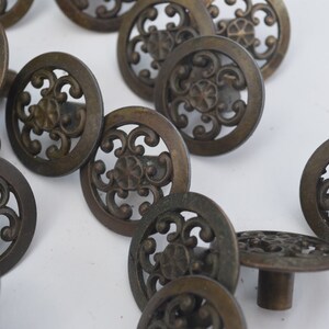 May include: A collection of ornate, round, bronze cabinet knobs with a decorative, floral design.