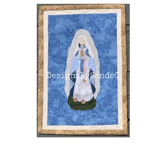 Pode incluir: Uma tapeçaria de parede acolchoada azul e branca com uma imagem da Virgem Maria, também conhecida como Nossa Senhora de Guadalupe, com uma coroa dourada e uma túnica azul. O fundo é um padrão floral azul.