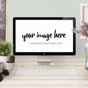 May include: A white desktop computer with a blank screen displaying the text "your image here" and the website address "pixeldustdesignstudio.com". The computer is on a white desk with a keyboard, a calendar, a stack of books, a pair of sunglasses, a potted plant, a vase of purple flowers, and a metal organizer.