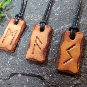 May include: Four leather pendants with black cords, each featuring a different rune symbol. The runes are carved into the leather and are visible against the brown background.