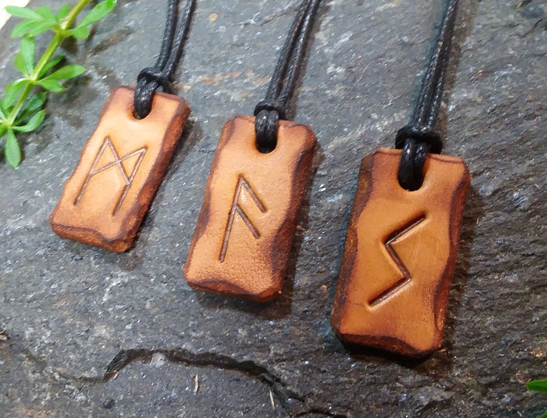 May include: Four leather pendants with black cords, each featuring a different rune symbol. The runes are carved into the leather and are visible against the brown background.