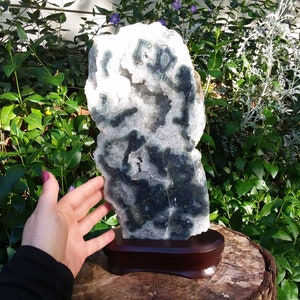 May include: A large, white and green agate geode with a natural, rough exterior. The geode is displayed on a wooden stand.