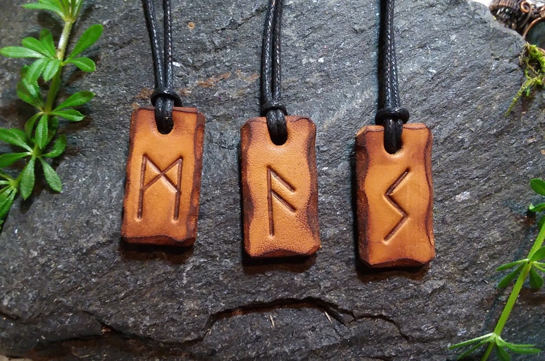 May include: Three leather pendants with black cords, each featuring a different Norse rune symbol. The runes are etched into the leather and are visible against the brown background.