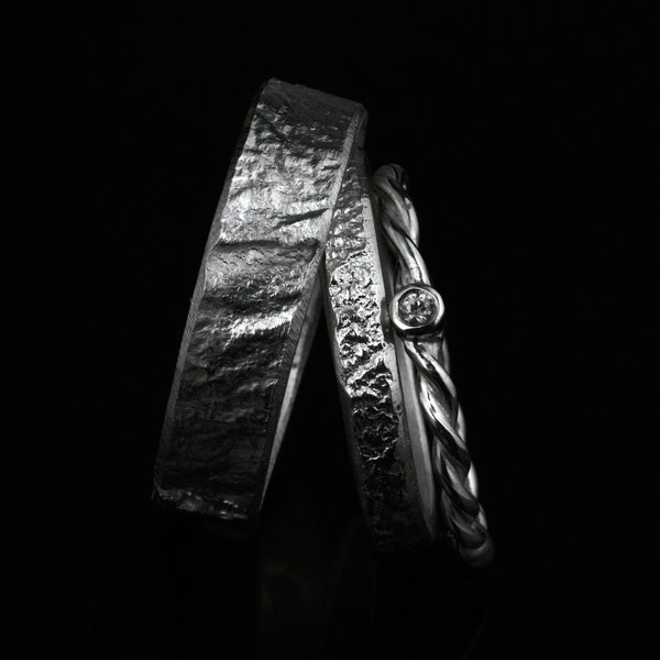 May include: Two silver wedding bands, one with a textured finish and the other with a braided design, featuring a small diamond.