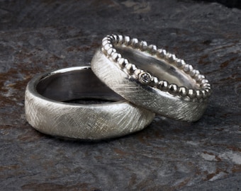 May include: Two silver wedding bands, one with a beaded edge and a small diamond, the other with a textured finish.