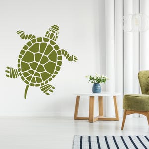 May include: Olive green turtle wall decal. The turtle is depicted in a stylized, geometric design, with a segmented shell and flipper-like limbs. The decal is applied to a white wall, creating a decorative accent.