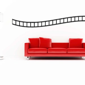 Könnte beinhalten: Ein rotes Sofa mit zwei Kissen steht vor einer weißen Wand mit einem schwarzen Filmstreifen-Design.