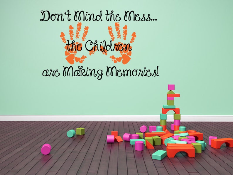 Making memories wall decal made with heart-shaped handprints and playful lettering. Handprint heart decal with the phrase “Don’t Mind the Mess the Children Are Making Memories” applied in vinyl. Kids wall decal featuring whimsical quote and handprint design made of hearts.