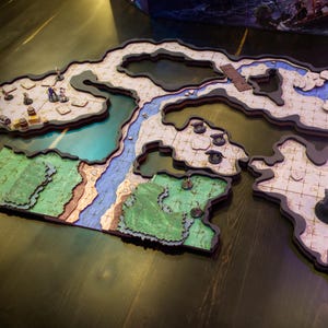 May include: A multi-piece, wooden tabletop gaming terrain set. The set features a detailed map with painted sections representing land, water, and sky. Miniature figures and game pieces are placed on the map, suggesting a role-playing game setting.