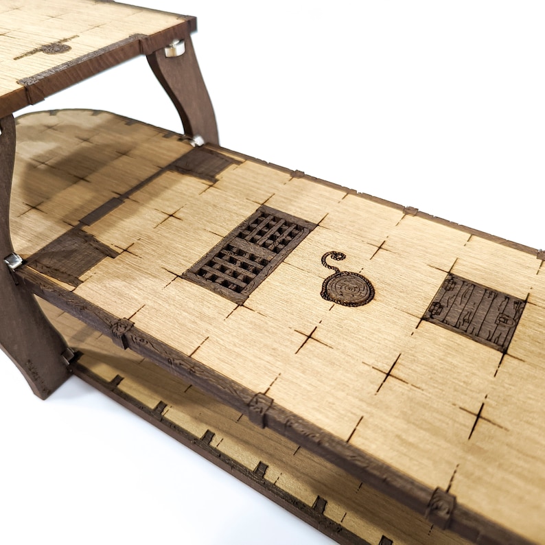 May include: A wooden model of a ship's deck with two levels. The top level features a small hatch and a circular design. The bottom level has a larger hatch and a rectangular design.