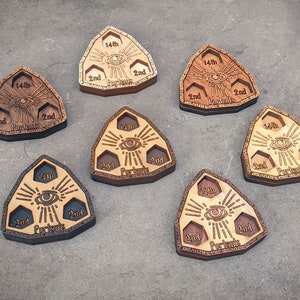 Puede incluir: Seis dados triangulares de madera con un diseño de ojo y el texto "14th Portents" y "2nd".