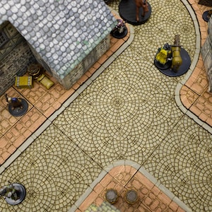 May include: A miniature tabletop game set with a cobblestone street, buildings, and figures. The street is made of a light brown material with a circular pattern. The buildings are made of a gray material with brown accents. The figures are made of a variety of materials, including plastic and metal.